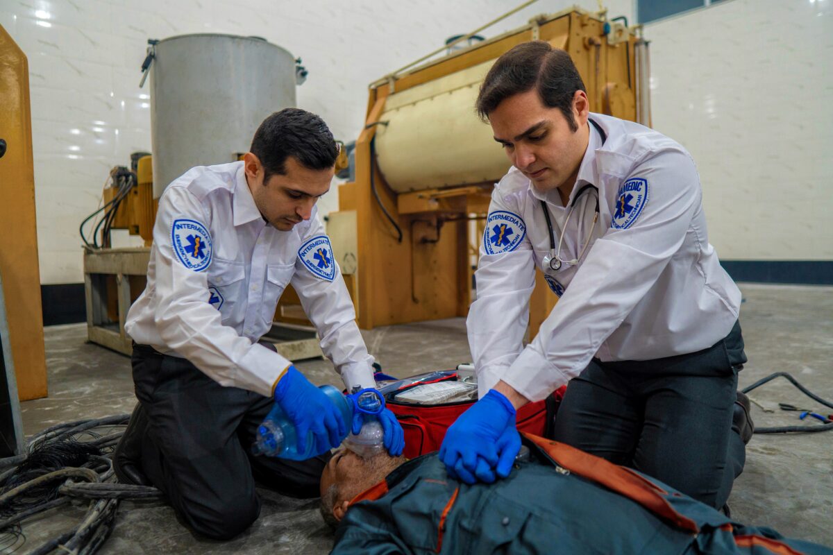 Two first responders and EMS staff in white uniform shirts and blue gloves perform CPR on a Electrocution victim. One is providing CPR, the other is using a bag valve mask.